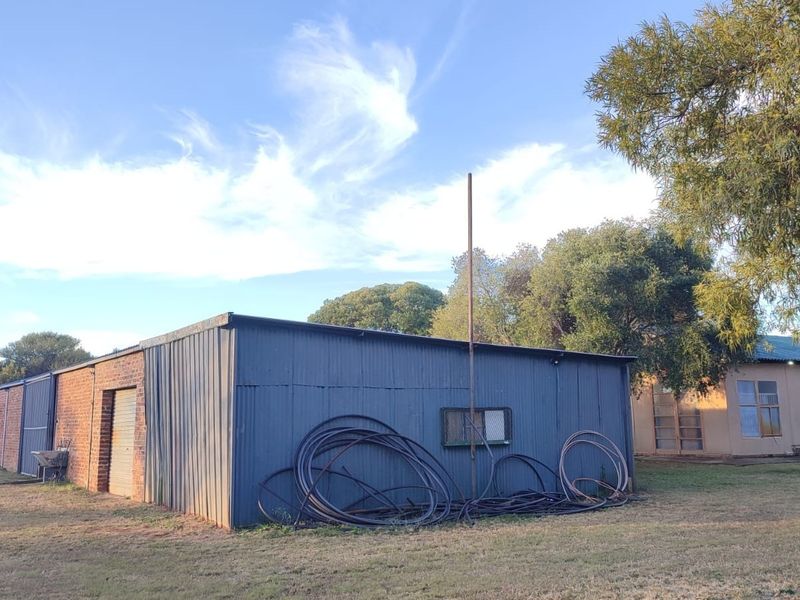 Exterior view of a farm outbuilding featuring corrugated metal cladding and brick masonry construction set within a rural landscape.