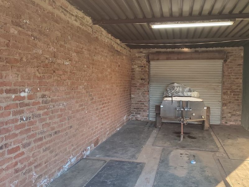 A functional garage space featuring exposed brick walls, a corrugated metal roof, and a secure roller shutter door.