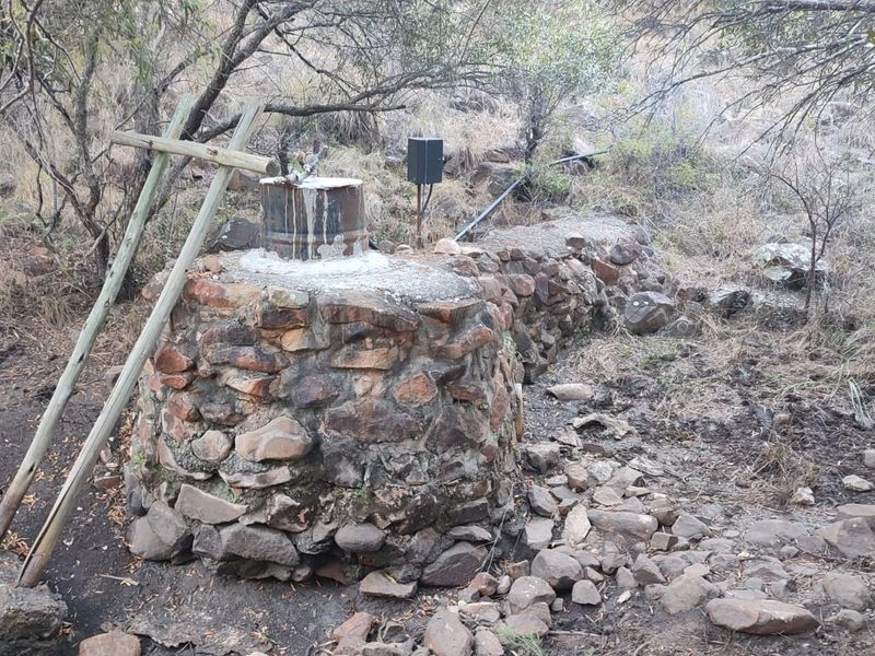 Outdoor utility area featuring a stone-built well structure with integrated water pump infrastructure and associated irrigation piping on the farm property.