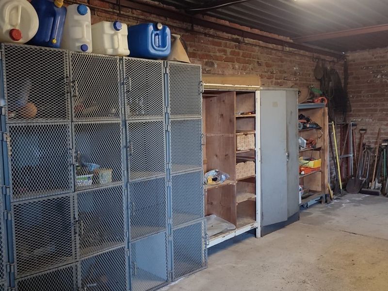 A functional utility or storage space featuring exposed brick walls, concrete flooring, and industrial-style metal storage lockers.