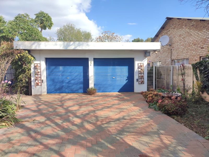 A double garage with blue roller doors and a paved driveway, situated in a residential setting with established garden borders.