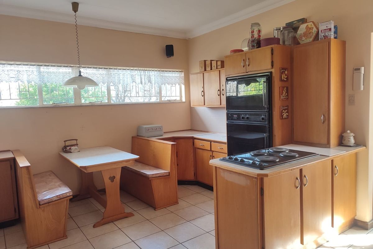 A dated kitchen featuring wooden cabinetry, a built-in oven, electric cooktop, and a fixed breakfast nook with tiled flooring.
