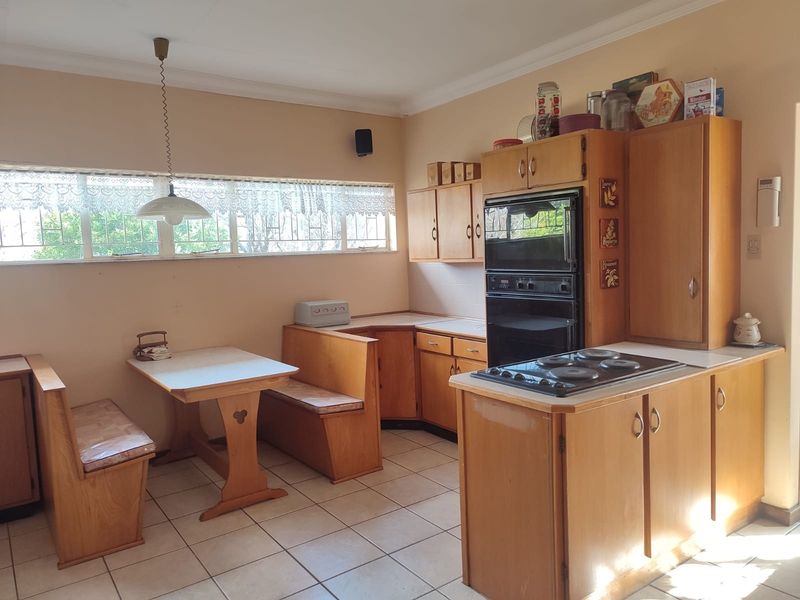 A dated kitchen featuring wooden cabinetry, a built-in oven, electric cooktop, and a fixed breakfast nook with tiled flooring.