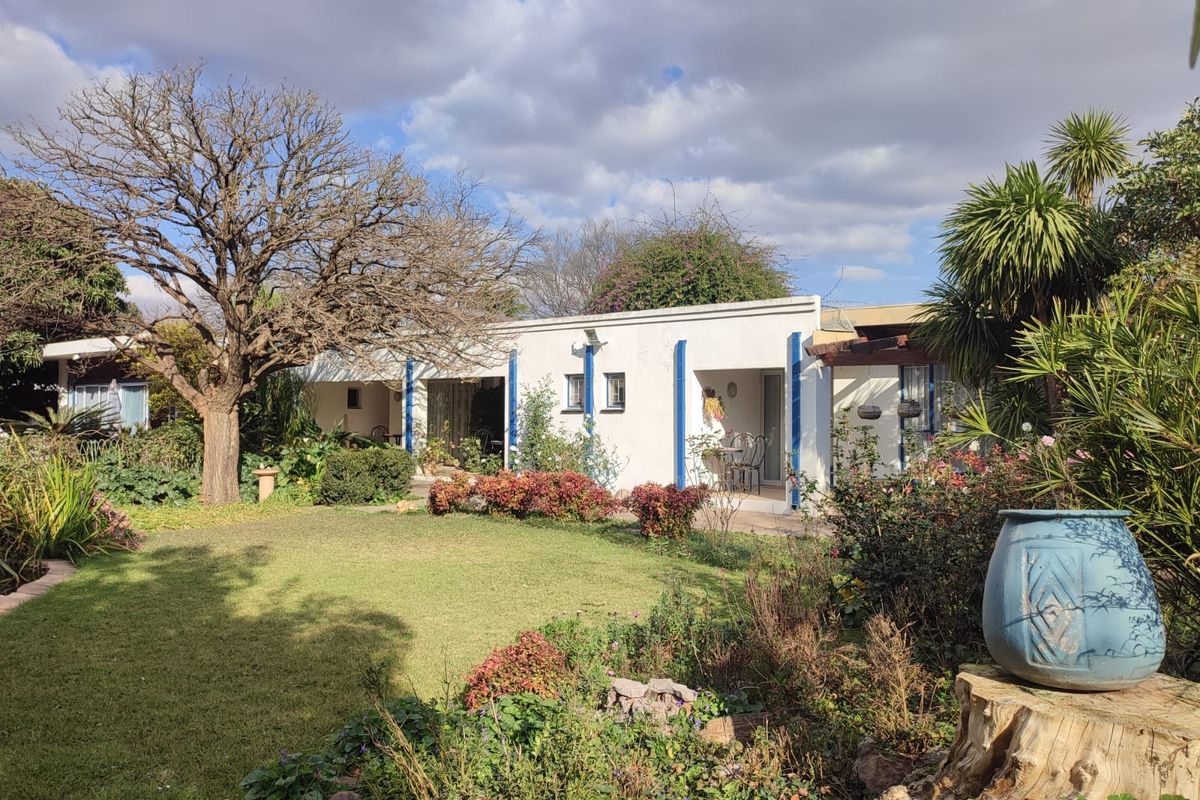 A view of the rear facade of the house featuring a covered patio area overlooking a well-maintained garden with mature trees and shrubs.