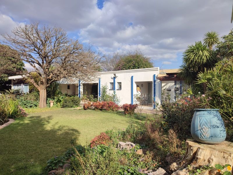 A view of the rear facade of the house featuring a covered patio area overlooking a well-maintained garden with mature trees and shrubs.