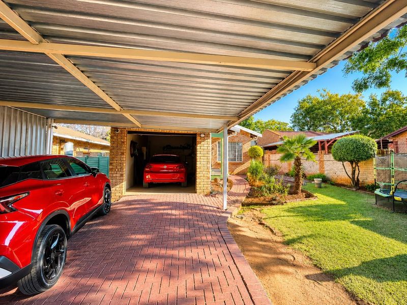 A functional brick garage with an attached corrugated metal carport, featuring a paved driveway and a well-maintained garden area.
