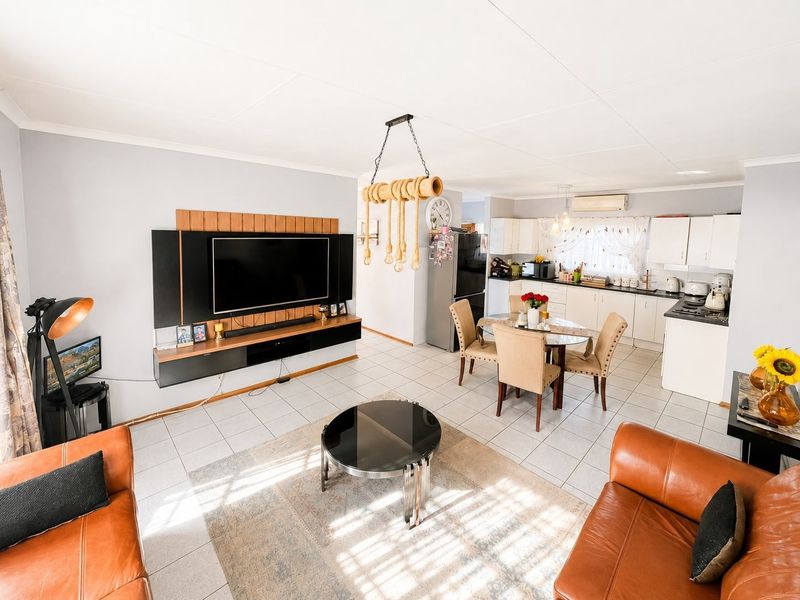 Open-plan living and dining area featuring tiled floors, a modern built-in media unit, and a functional kitchen with ample cabinetry.