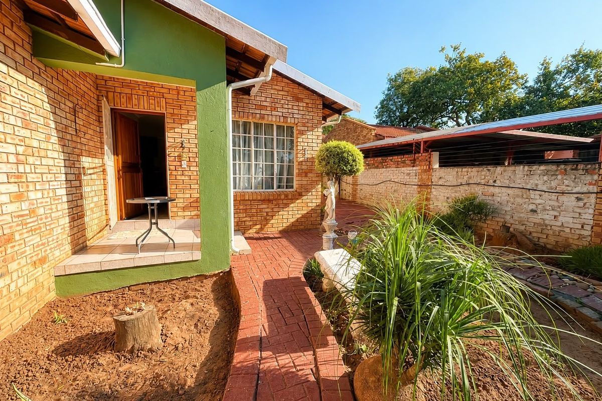 Rear exterior view featuring a brick facade, tiled patio entrance, and a paved pathway leading through the garden area with boundary walling.