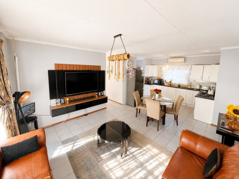 An open-plan living and kitchen area featuring tiled flooring, a modern wall-mounted entertainment unit, and a functional kitchen with white cabinetry.