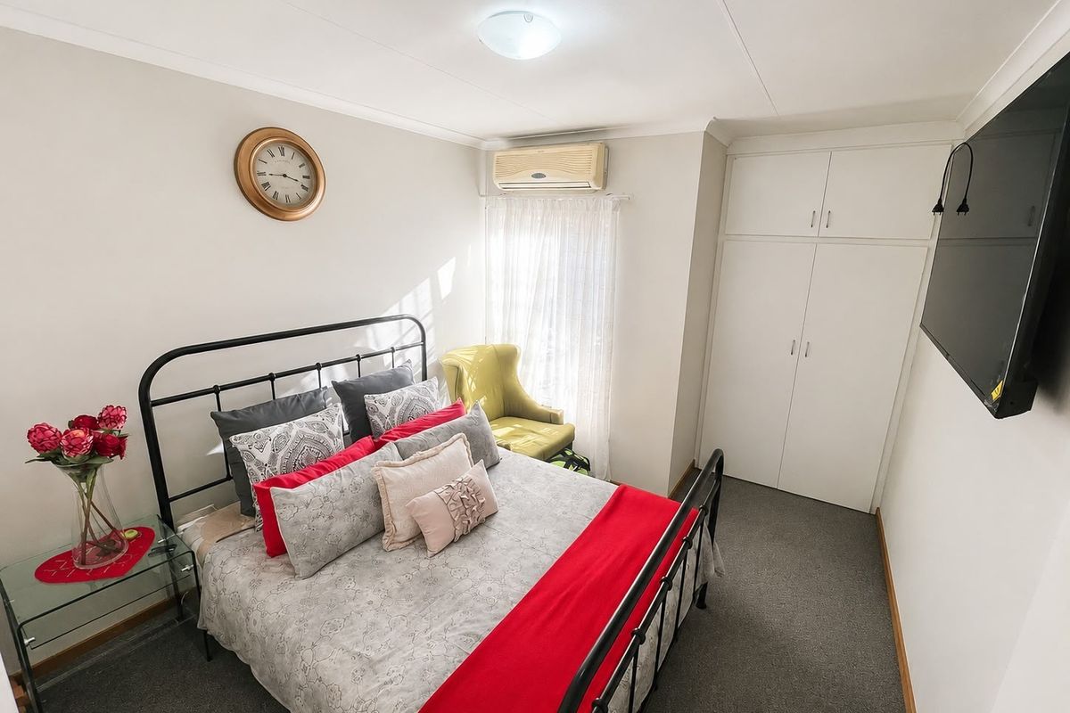 A well-maintained bedroom featuring built-in cupboards, wall-mounted air conditioning, and neutral carpeting.