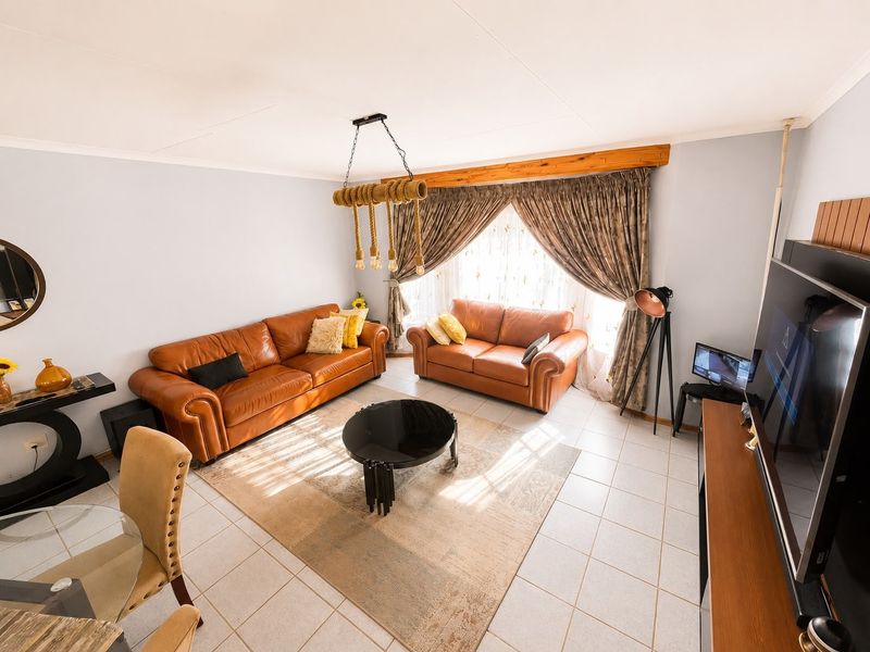 A well-lit living room featuring tiled flooring, a decorative pendant light fixture, and a timber window pelmet, offering a comfortable and functional living space.