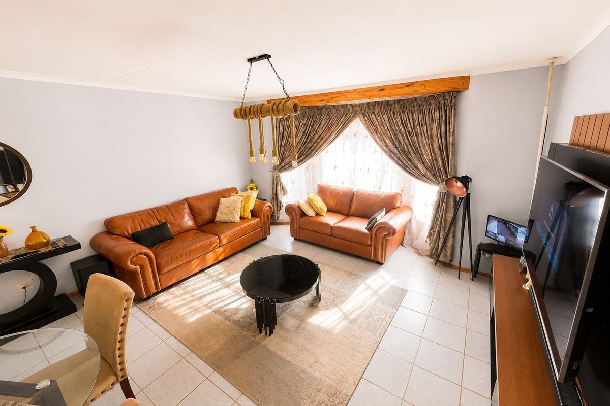 A well-lit living room featuring tiled flooring, a decorative pendant light fixture, and a timber window pelmet, offering a comfortable and functional living space.
