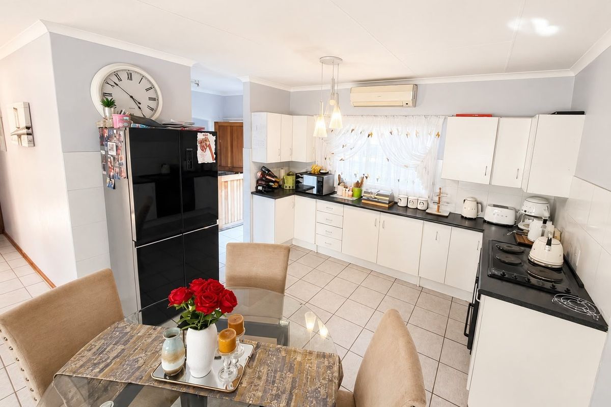 A functional kitchen featuring white cabinetry, dark countertops, an electric hob, and tiled flooring, with an integrated air conditioning unit.