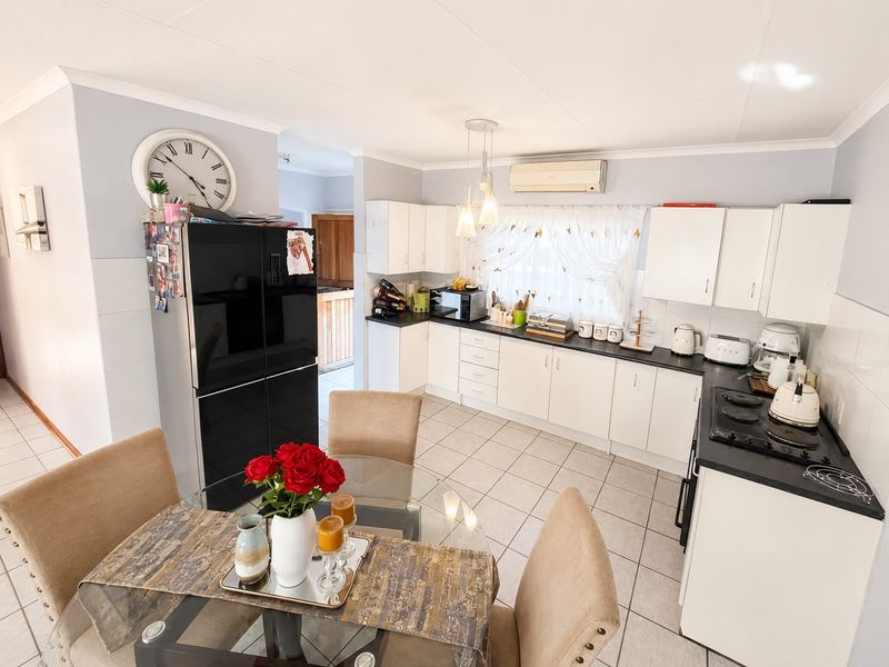A functional kitchen featuring white cabinetry, dark countertops, an electric hob, and tiled flooring, with an integrated air conditioning unit.