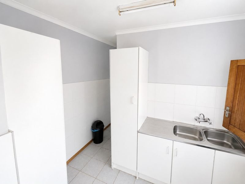 A functional laundry area featuring built-in white cabinetry, a stainless steel double sink, tiled splashback, and neutral tiled flooring.