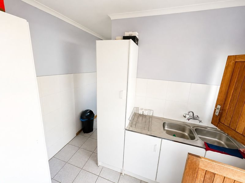 A functional laundry area featuring tiled flooring, a stainless steel double sink with mixer tap, and built-in storage cabinetry.