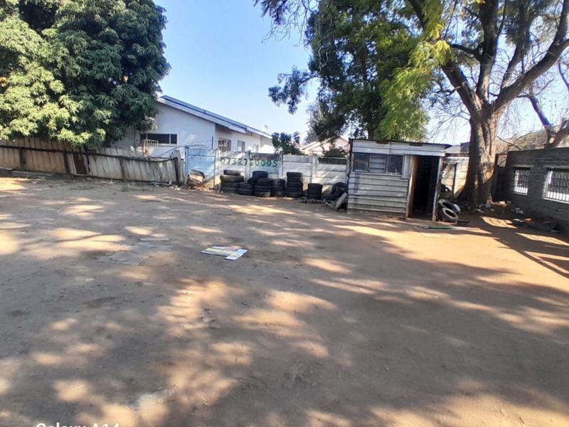 A view of a vacant residential plot featuring a metal shed, mature trees, and precast concrete boundary walling.