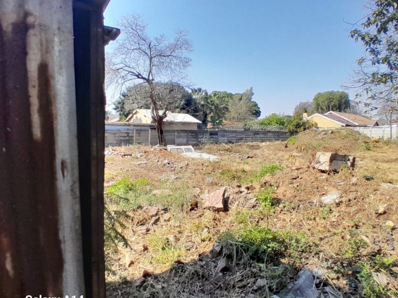 A view of a vacant residential plot featuring uneven terrain, overgrown vegetation, and a precast concrete boundary wall.