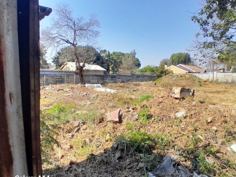 A view of a vacant residential plot featuring overgrown vegetation, debris, and perimeter walling, offering a blank canvas for future development.
