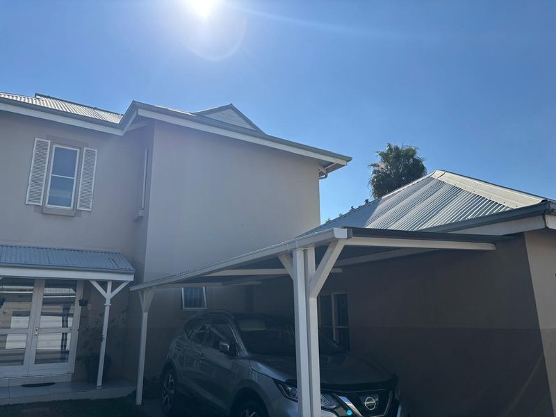 Front elevation of a townhouse featuring a covered carport, corrugated metal roofing, and double glass entrance doors.