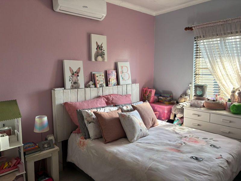A bedroom featuring a split-system air conditioner and venetian blinds, with pink and grey painted walls.