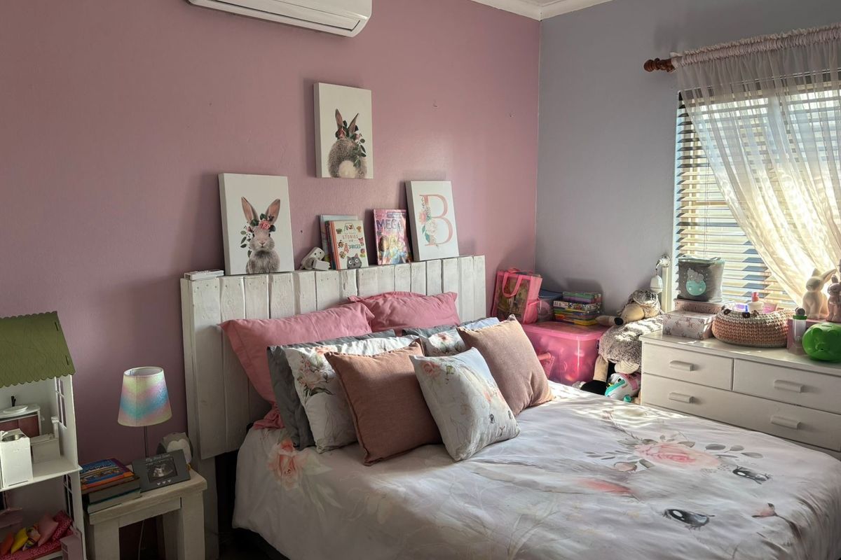 A bedroom featuring a split-system air conditioner and venetian blinds, with pink and grey painted walls.