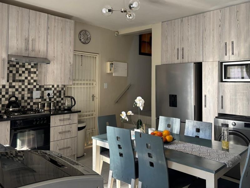Open-plan kitchen and dining area featuring wood-grain cabinetry, a gas hob, integrated appliances, and a modern tiled backsplash.
