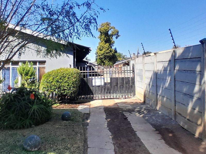 Front exterior view featuring a concrete driveway, metal security gate, and a precast concrete boundary wall with electric fencing.
