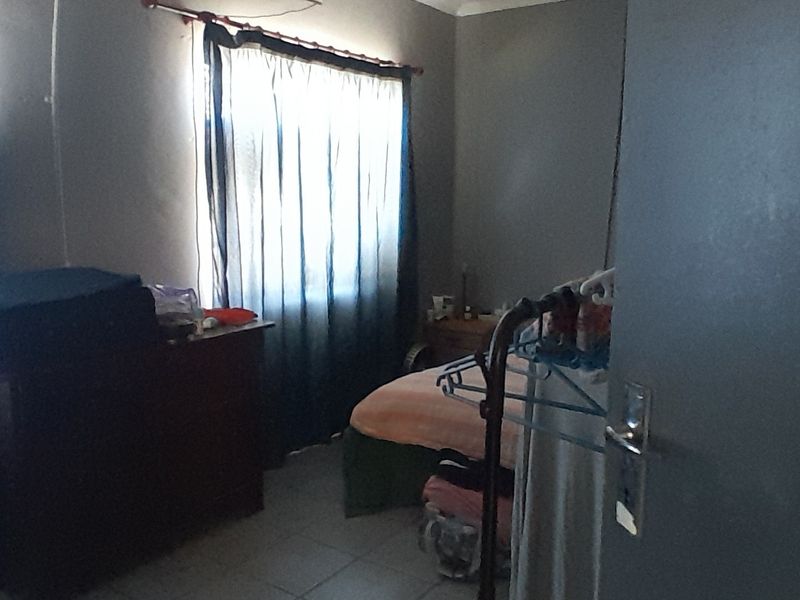 A standard bedroom featuring tiled flooring and a window with curtain rod, providing a functional space for rest.