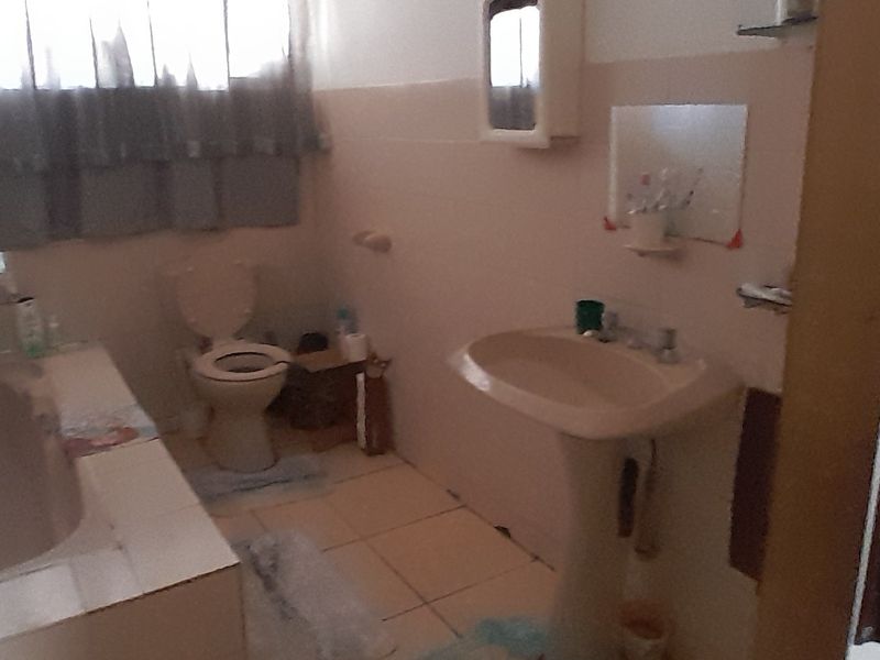 A dated bathroom featuring a pedestal sink, built-in bathtub, and toilet with neutral wall and floor tiling.