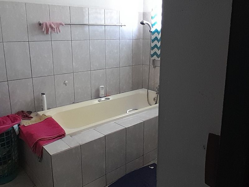 A functional bathroom featuring a built-in bathtub with wall-mounted shower fixtures and neutral ceramic wall tiling.