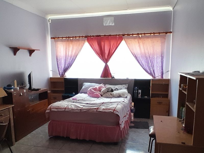 A bedroom featuring tiled flooring and a large window with curtain rods, offering a functional space for rest.