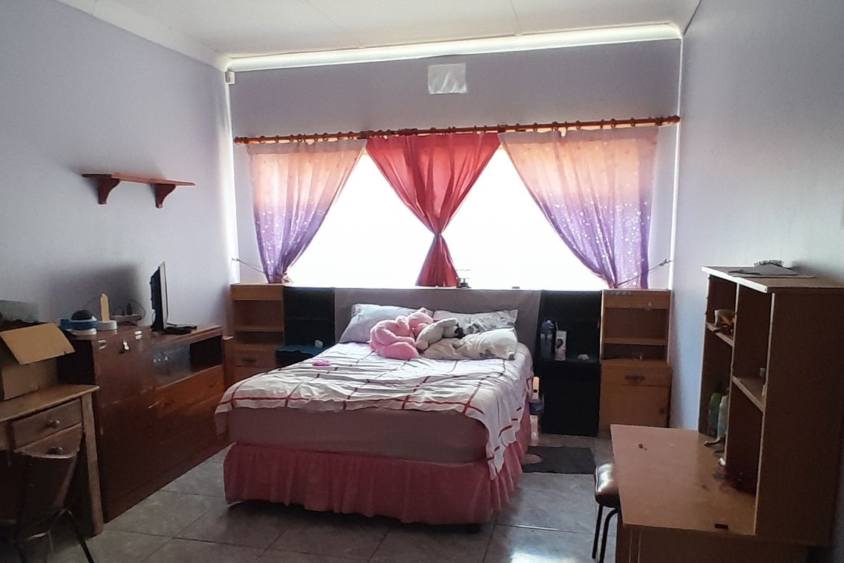 A bedroom featuring tiled flooring and a large window with curtain rods, offering a functional space for rest.