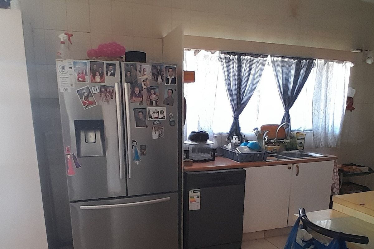A functional kitchen area featuring a stainless steel refrigerator, dishwasher, sink, and tiled backsplash, offering potential for modernization and aesthetic updates.