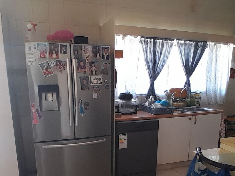 A functional kitchen area featuring a stainless steel refrigerator, dishwasher, sink, and tiled backsplash, offering potential for modernization and aesthetic updates.