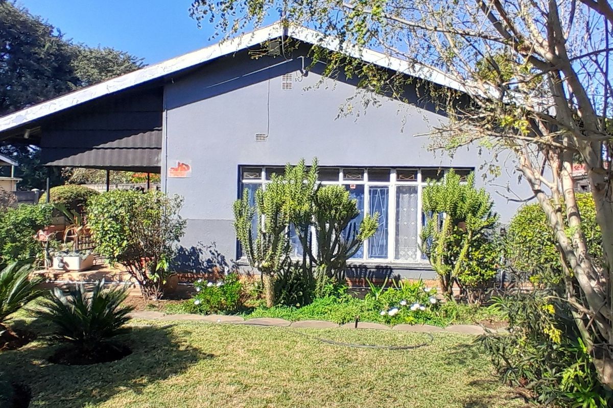 Rear view of the property featuring a garden, covered patio area, and a single-story structure with metal-framed windows and security bars.