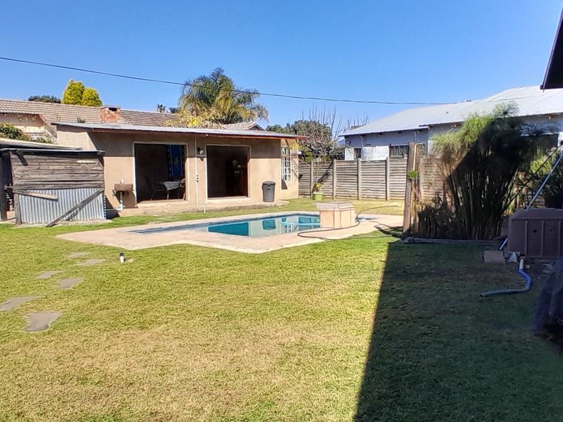 Rear garden area featuring a swimming pool with concrete surround, lawn, and perimeter boundary walling.