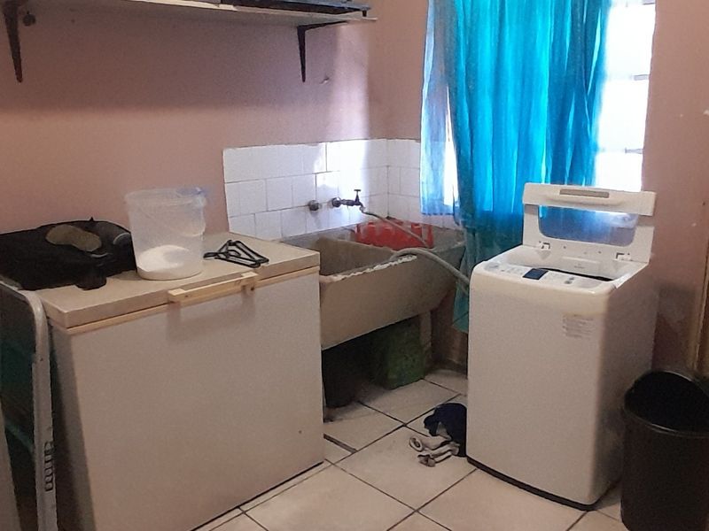 A functional laundry area featuring a traditional concrete sink, tiled splashback, and ceramic floor tiles, providing a practical space for utility and washing tasks.