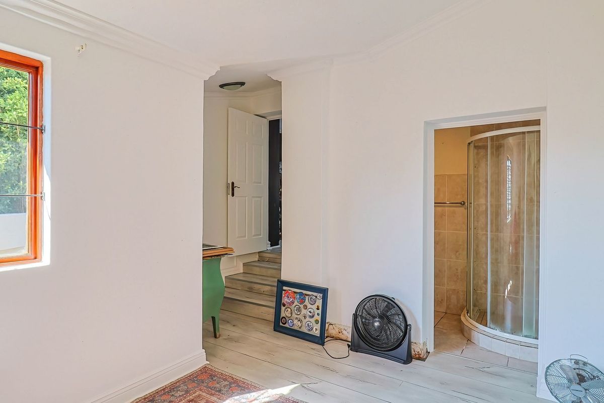 A bedroom featuring an en-suite shower, timber window frame, and neutral finishes, requiring minor repairs to the wall base and flooring.