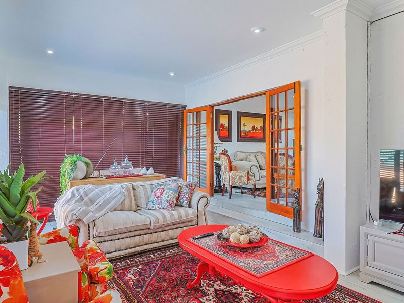 A bright living room featuring recessed downlights, crown molding, and wooden french doors leading to an adjacent space, complemented by venetian blinds.