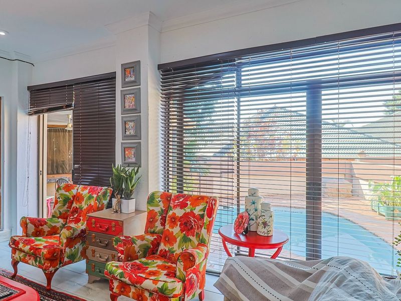 A bright living room featuring large sliding glass doors with venetian blinds, providing direct access to the outdoor pool area.