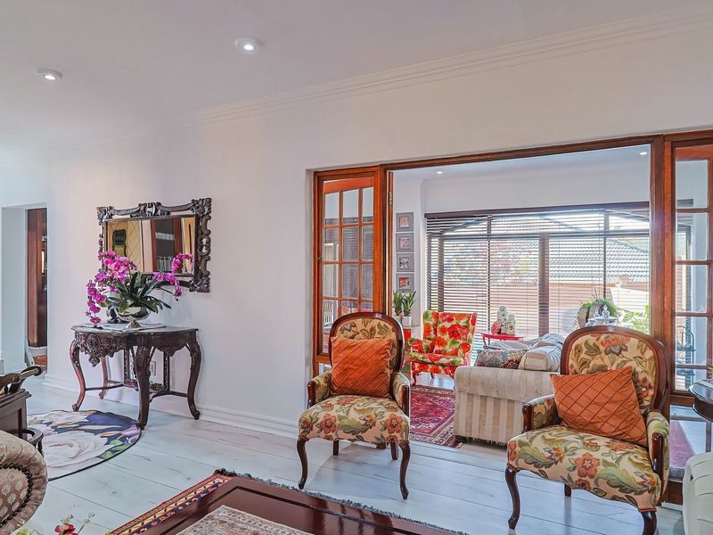 Spacious living area featuring timber flooring, recessed downlights, and elegant wooden door frames leading to an adjoining sunroom or patio space.