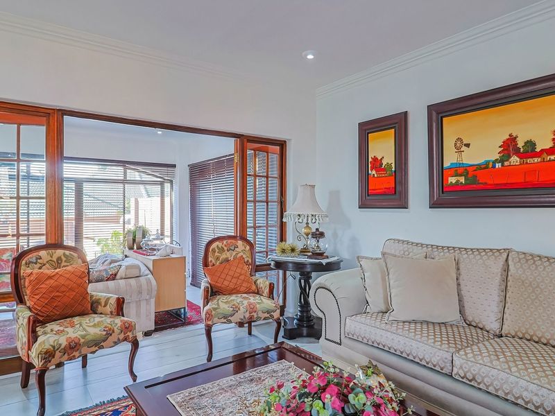 A bright living room featuring crown molding, recessed lighting, and large wooden-framed glass sliding doors that open to an adjacent sunroom or patio area.