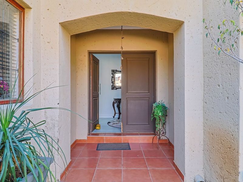 A welcoming townhouse entrance featuring a covered porch with terracotta tiling, an arched doorway, and a solid timber front door.