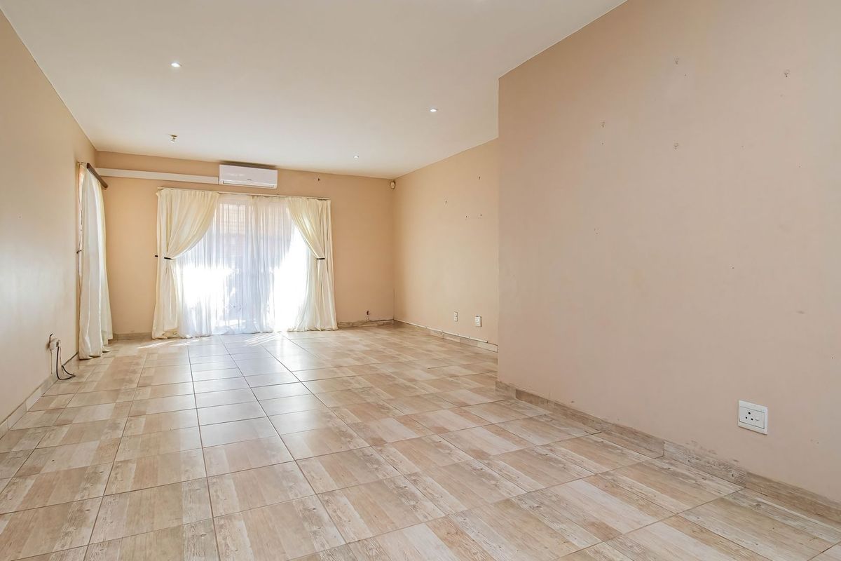 A spacious, empty living area featuring neutral tiled flooring, recessed lighting, a wall-mounted air conditioning unit, and sliding glass doors leading to the exterior.