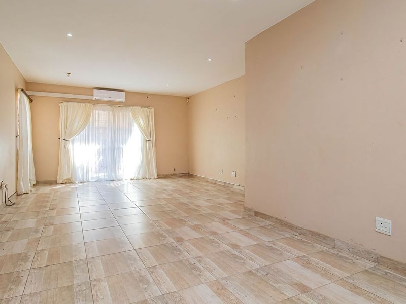 A spacious, empty living area featuring neutral tiled flooring, recessed lighting, a wall-mounted air conditioning unit, and sliding glass doors leading to the exterior.