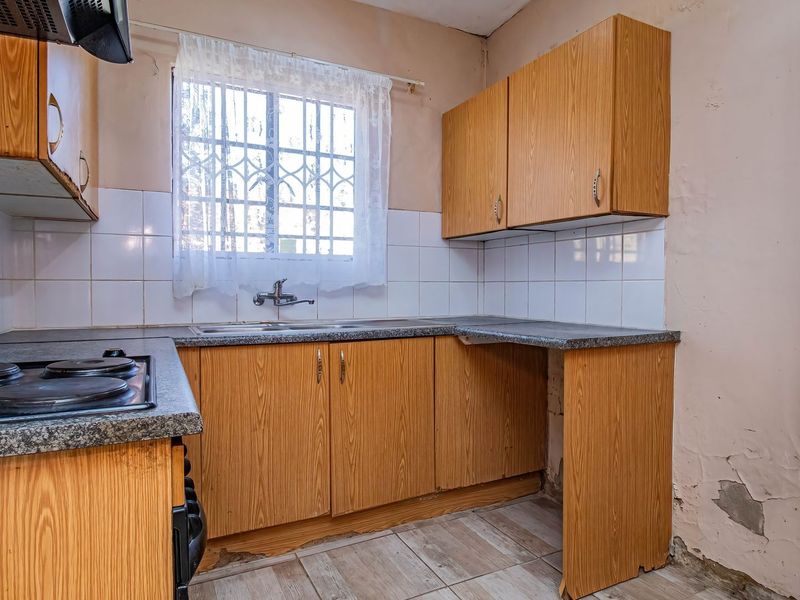 A dated kitchen featuring laminate cabinetry, a built-in electric hob, and a stainless steel sink, requiring cosmetic updates and wall repairs.