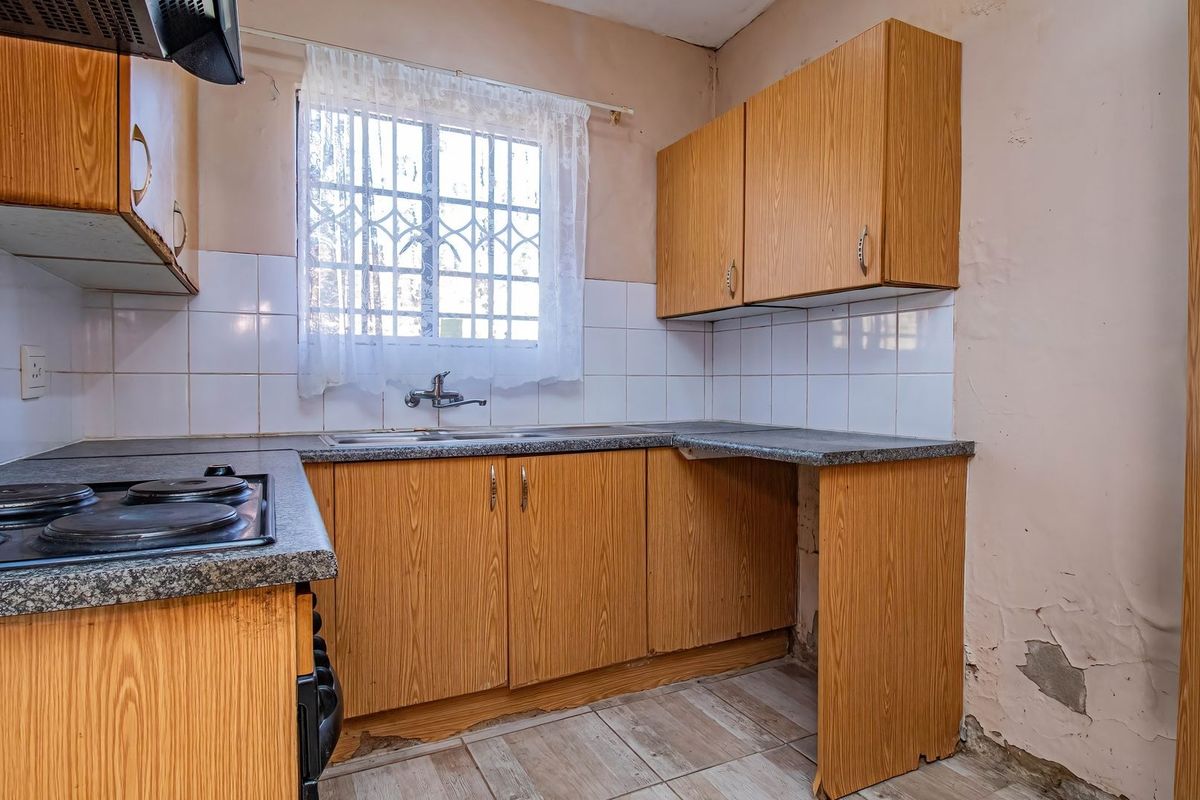 A dated kitchen featuring laminate cabinetry, a built-in electric hob, and a stainless steel sink, requiring cosmetic updates and wall repairs.