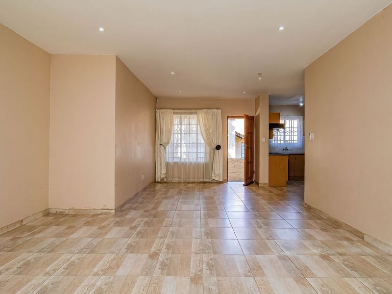 Spacious open-plan living area featuring neutral wall tones, ceramic tiled flooring, recessed lighting, and direct access to the exterior through a secure door.