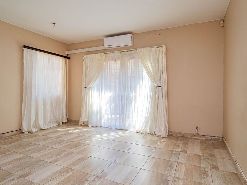 An empty living room featuring tiled flooring, a wall-mounted air conditioning unit, and access to an outdoor area via sliding glass doors.